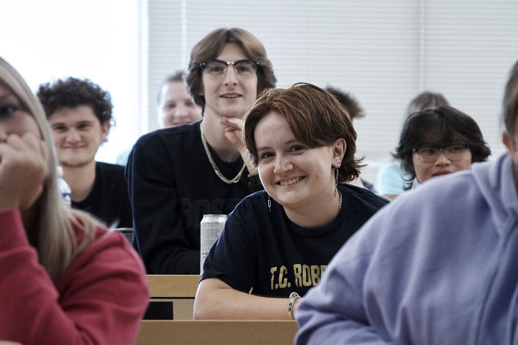 Female student smiles into camera while sitting in lecture hall