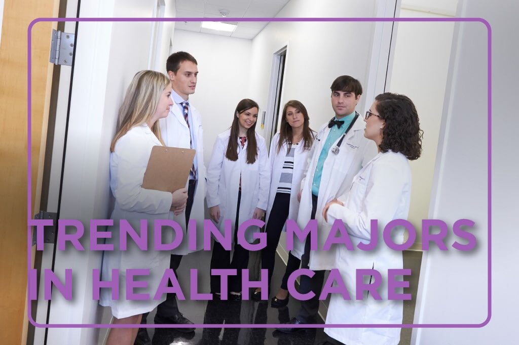 Group of students in white coats chat in an exam room hallway