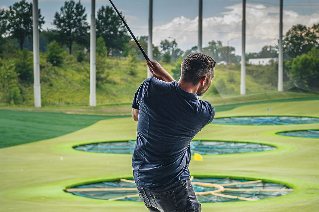 Man swings golf club in front of driving bay at Top Golf.